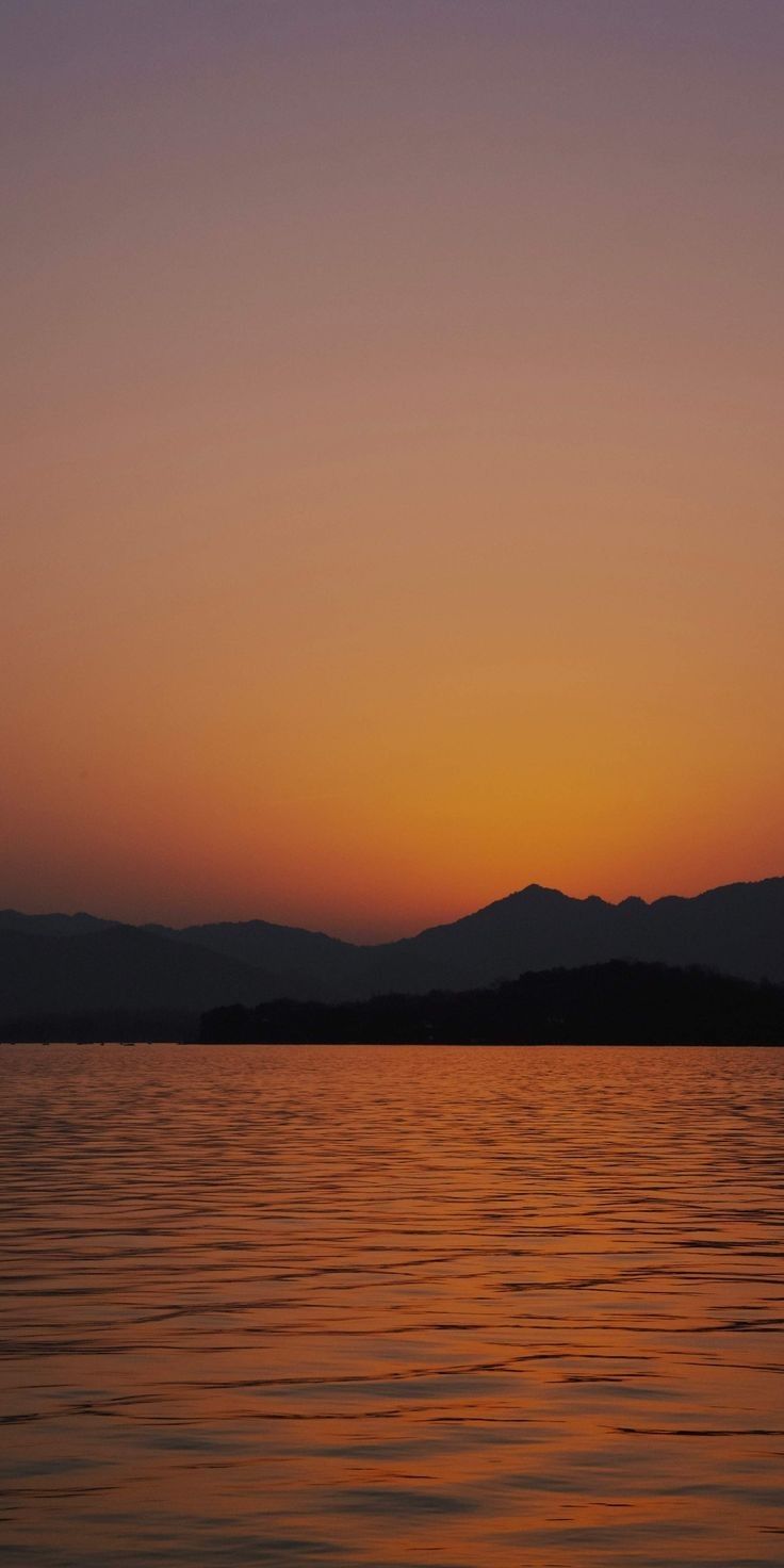 the sun is setting over water with mountains in the background