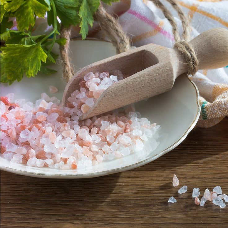 sea salt on a white plate next to a wooden spoon and green plant sprig