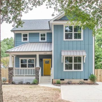 a blue house with a yellow door in the front yard and trees around it on a sunny day