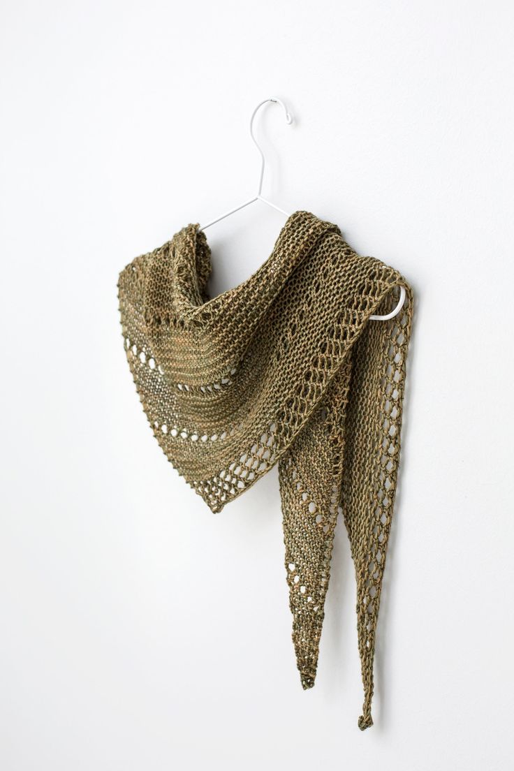 a crocheted shawl hanging on a white wall next to a hanger