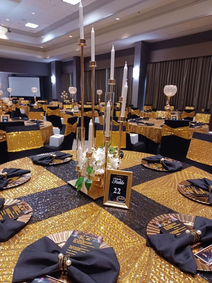 the tables are set up with black and gold linens, place settings, and candles