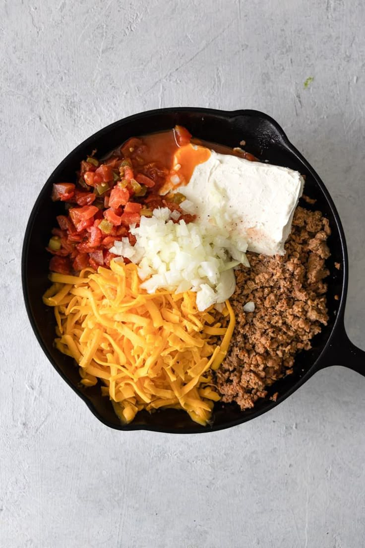 a skillet filled with cheese, ground beef and other ingredients to make an enchilada