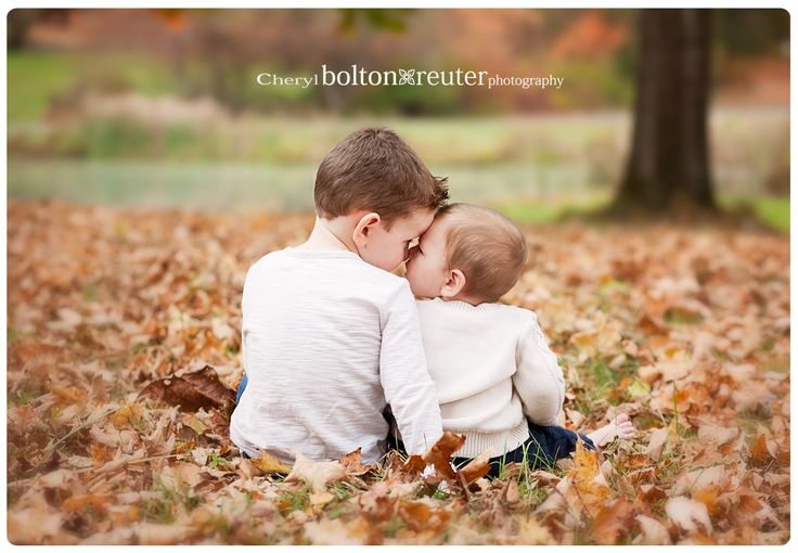 two young boys sitting in the leaves with their heads on each other's shoulders