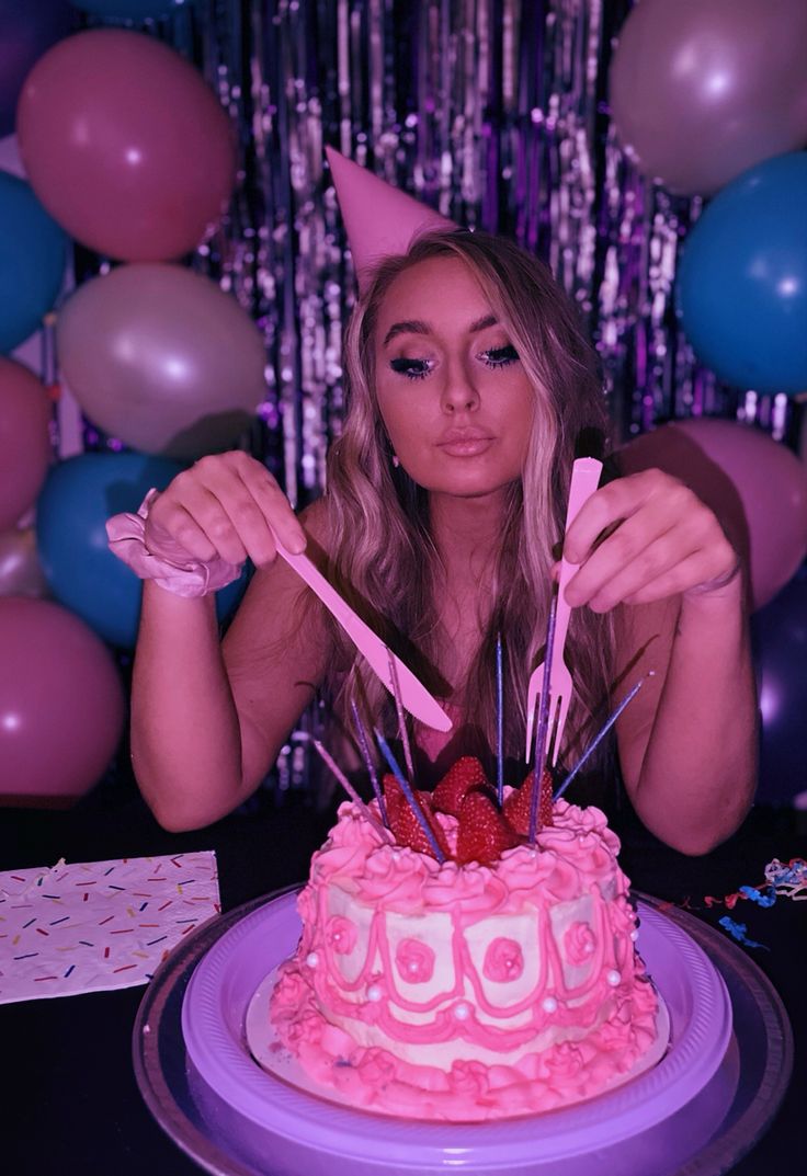 a woman sitting in front of a cake with candles and strawberries on it, surrounded by balloons