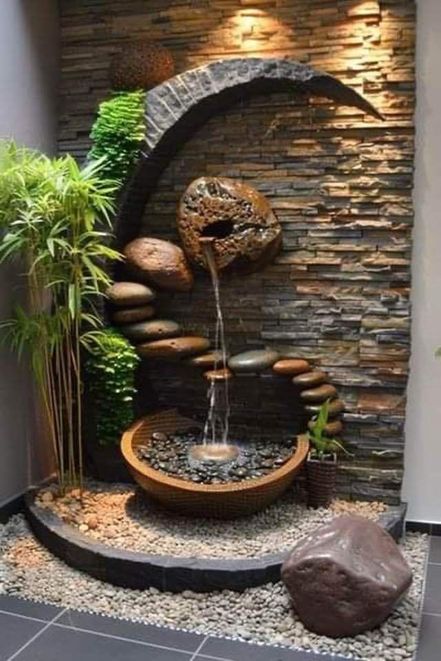 an outdoor fountain in the middle of a room with rocks and plants on top of it