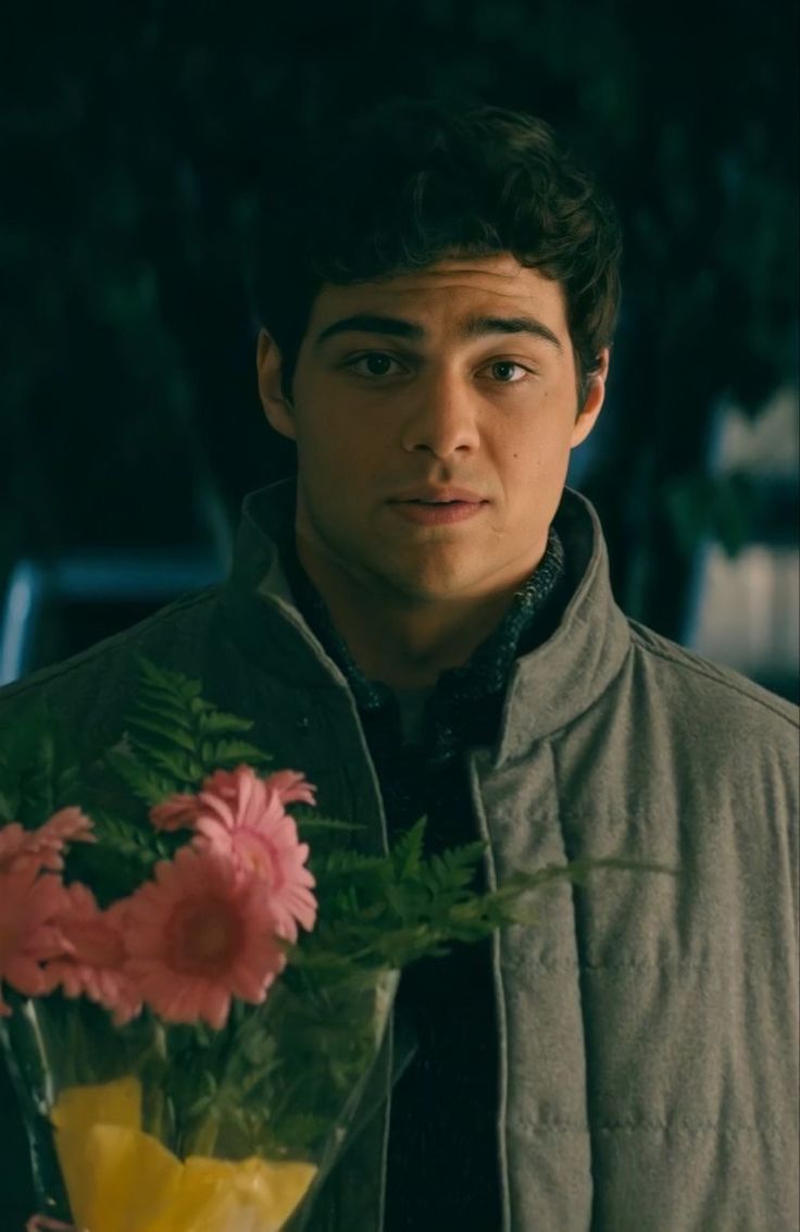 a young man holding a bouquet of flowers in his right hand and looking at the camera