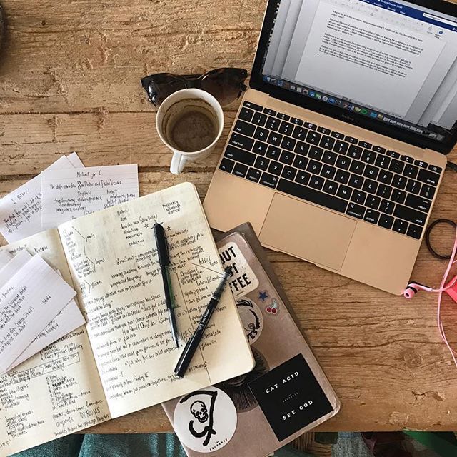 an open laptop computer sitting on top of a wooden table next to a pile of papers