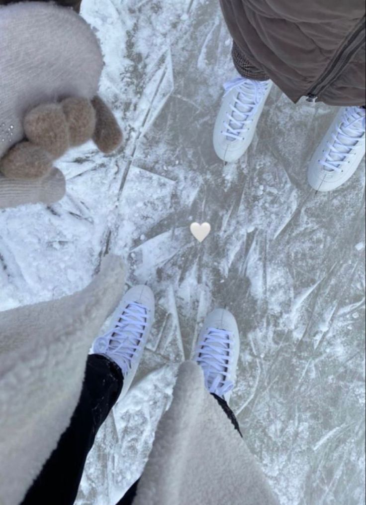 two people are standing in the snow with their feet up and one is holding a teddy bear