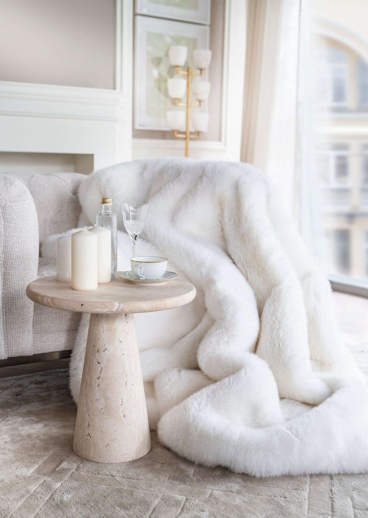 a white fur blanket sitting on top of a table next to a chair and window