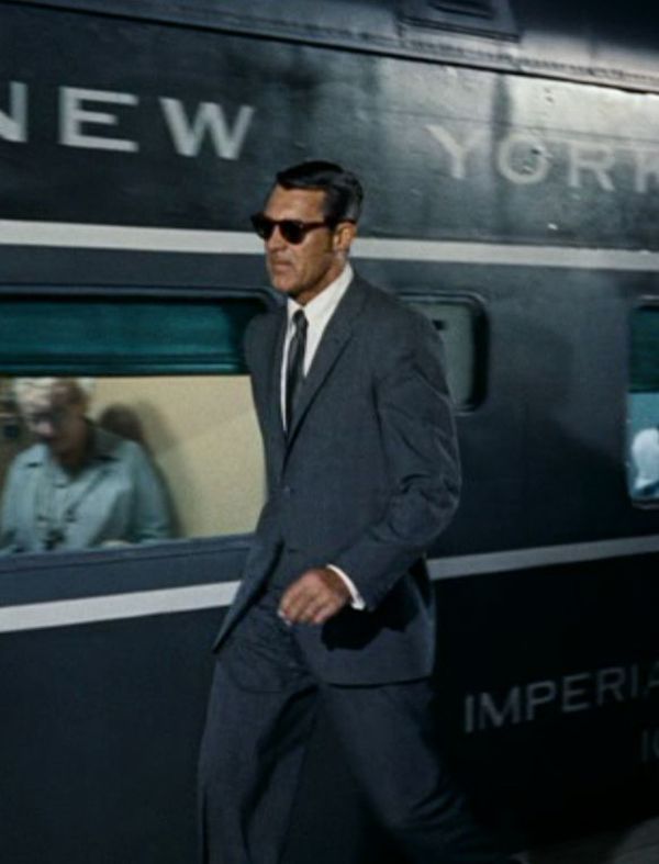 a man in a suit and sunglasses walking next to a train car with the word new york on it