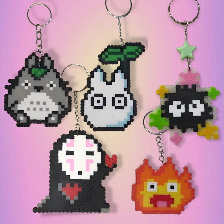 four pixel keychains are hanging on a pink background, each with different characters