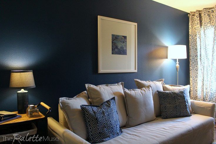 a living room with blue walls and white couches in front of a lamp on a table