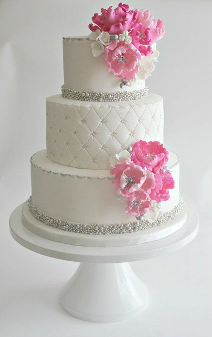 a three tiered cake with pink flowers on the top and diamond trimmings