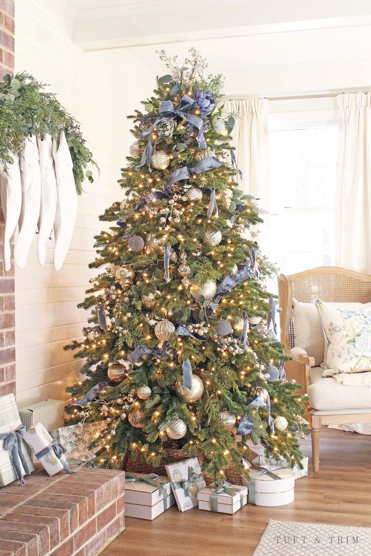 a decorated christmas tree with blue and silver ornaments in a living room area next to a fireplace