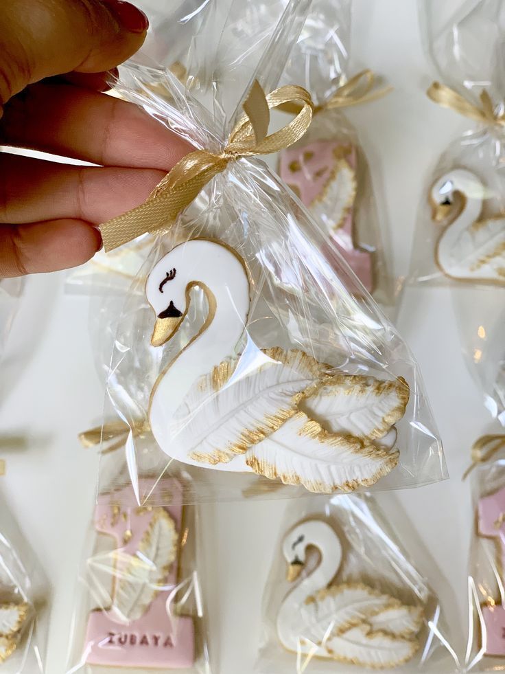 a hand holding a white swan shaped cookie in front of some cookies wrapped in cellophane