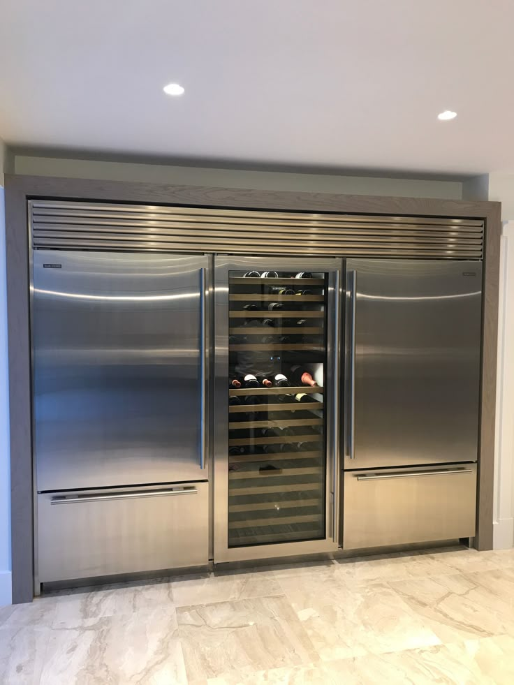 a stainless steel double door refrigerator with wine bottles in the bottom drawer and shelves on both sides