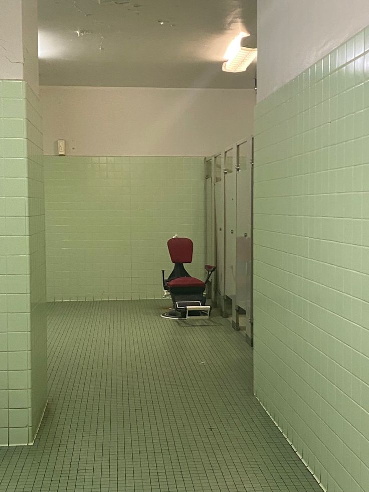 an empty room with green tiles and a red chair in the middle of the hallway