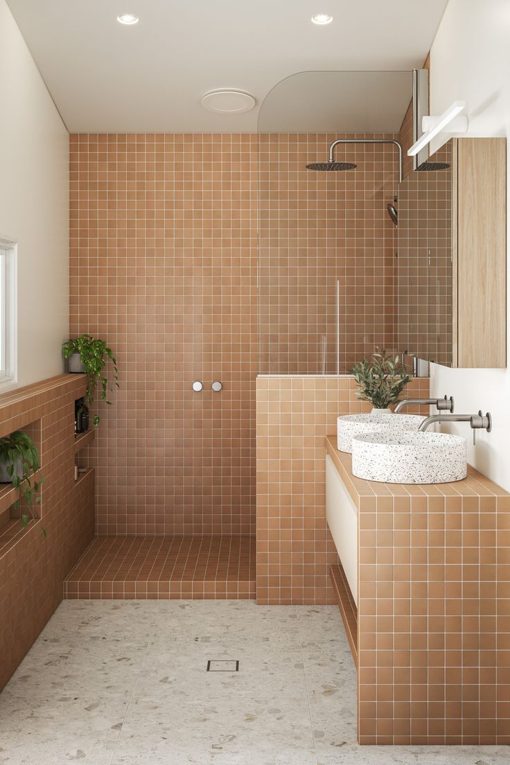 a tiled bathroom with two sinks and a walk in shower next to a plant on the counter