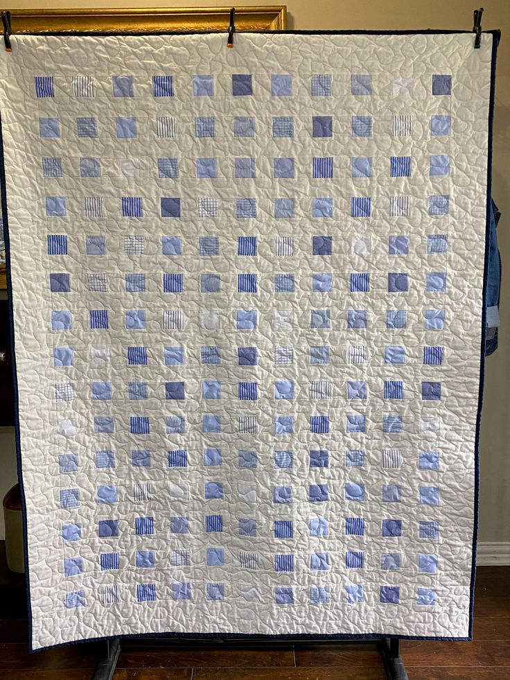 a white quilt with blue squares on it sitting on top of a wooden floor next to a wall