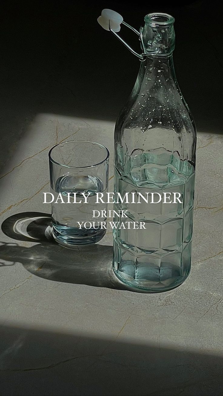 a glass and bottle sitting next to each other on a table with the words daily reminder drink your water