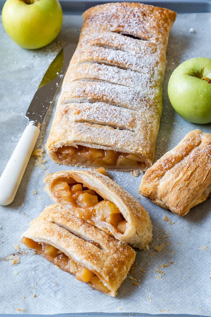 an apple pie is cut in half and sitting next to some apples on the table