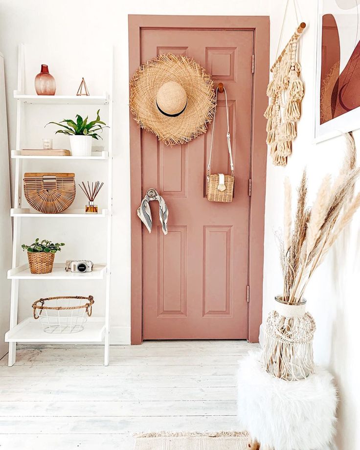 a pink door in a white room with baskets and hats hanging on the wall next to it