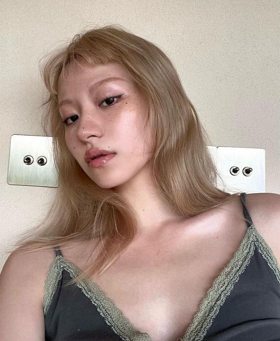 a woman with long blonde hair wearing a gray bra and posing in front of a light switch