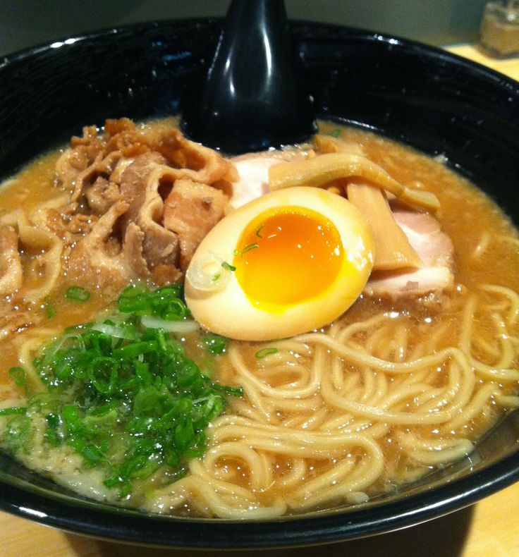 a bowl filled with noodles, meat and an egg in it's center on top of a wooden table