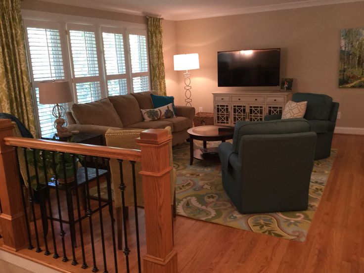 a living room filled with furniture and a flat screen tv mounted on the wall above a wooden banister