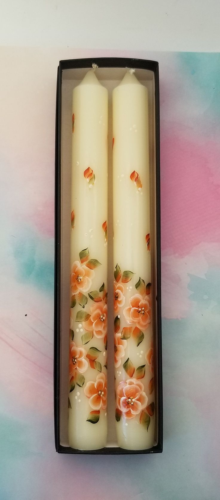 two white candles with orange flowers in a black box on top of a colorful background