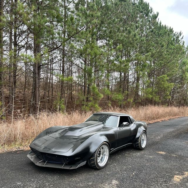 a black car is parked on the side of the road in front of some trees