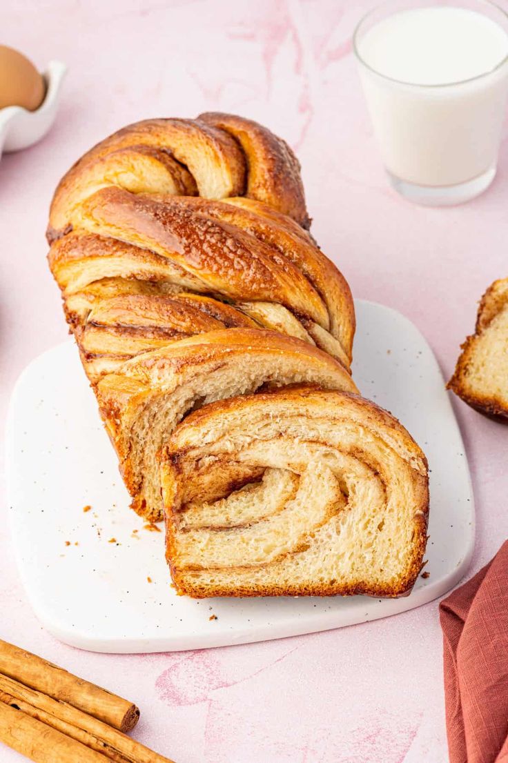 a loaf of cinnamon roll sitting on top of a white plate next to some cinnamon sticks