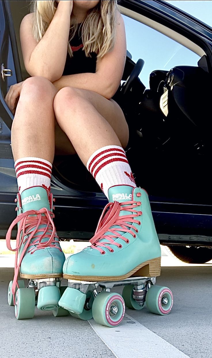 a woman sitting on top of a skateboard in front of a car with her legs crossed