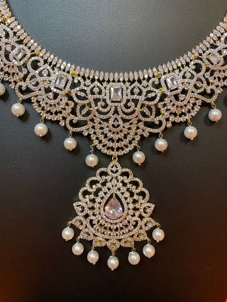 Indulge in luxury with our exquisite South Indian Haaram necklace. Adorned with CZ American Diamonds, it is the perfect accessory for weddings, parties, and gifting. Elevate your Indian outfit, be it a silk saree or gown, with this long and elegant necklace. A must-have for every sophisticated and exclusive wardrobe. This jewellery set includes a necklace and matching earrings. Jewellery Care- Keep the jewellery dry, avoid contact with perfumes and water. Dazzling Bridal Necklace For Festive Occasions, Elegant American Diamond Bridal Necklace For Festive Occasions, Festive Dazzling Bridal Necklace, Elegant Bridal Necklace With Stone Work For Festive Occasions, Elegant Lehenga With Intricate Design For Diwali, Dazzling Bridal Necklace For Festive Party, Dazzling Festive Bridal Necklace For Party, Festive Crystal Necklaces For Reception, Crystal Kundan Necklace With Stone Work For Wedding