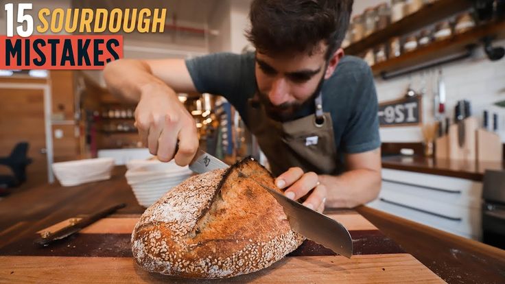 a man cutting up a loaf of bread on top of a wooden counter next to a knife