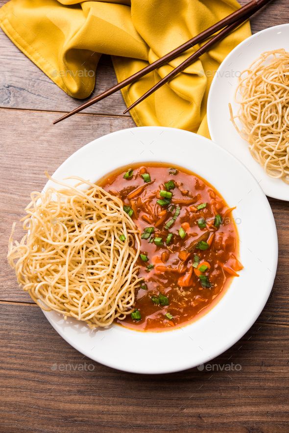 two white plates filled with noodles and sauce on top of a wooden table next to chopsticks