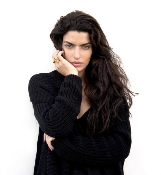 a woman with long dark hair posing for a photo in front of a white wall