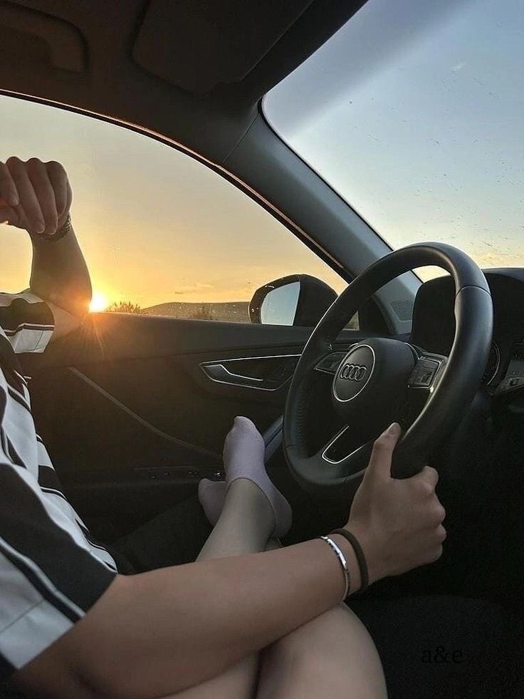 a woman driving a car with the sun setting in the background and her hand on the steering wheel