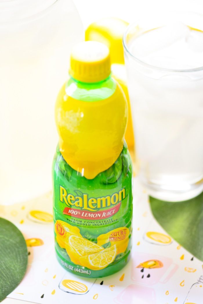 a bottle of real lemon juice next to a glass of water on a tablecloth