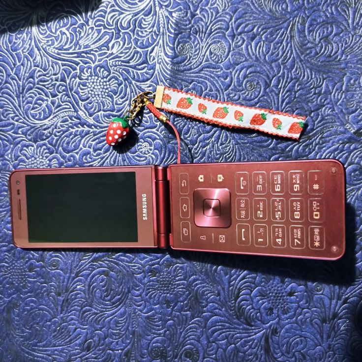 an old cell phone with a key chain attached to it sitting on top of a bed