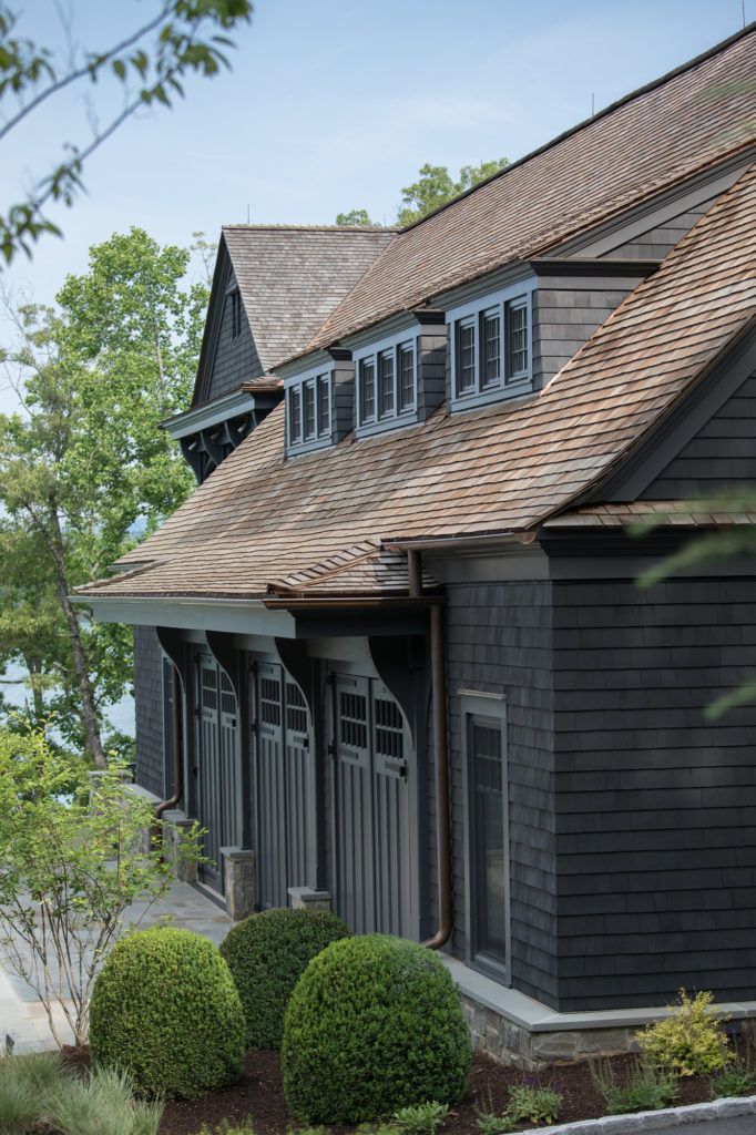 a black house with brown shingles on the roof and two large bushes in front of it