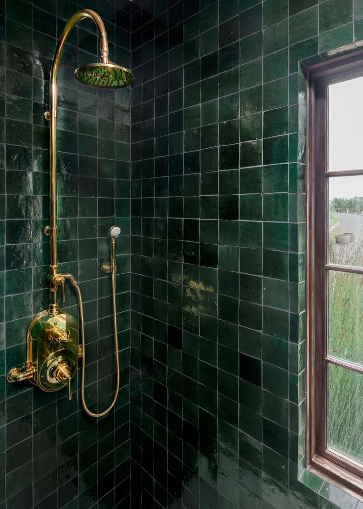 a green tiled bathroom with a gold shower head and hand held shower faucet