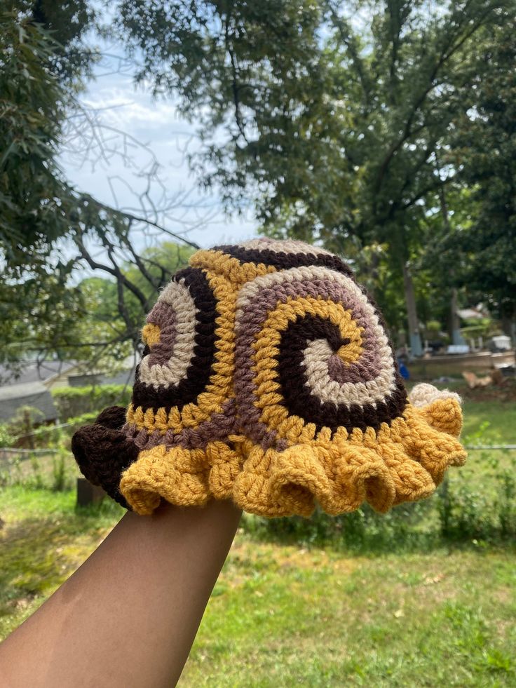 a crocheted hat is being held by someone's hand in the grass