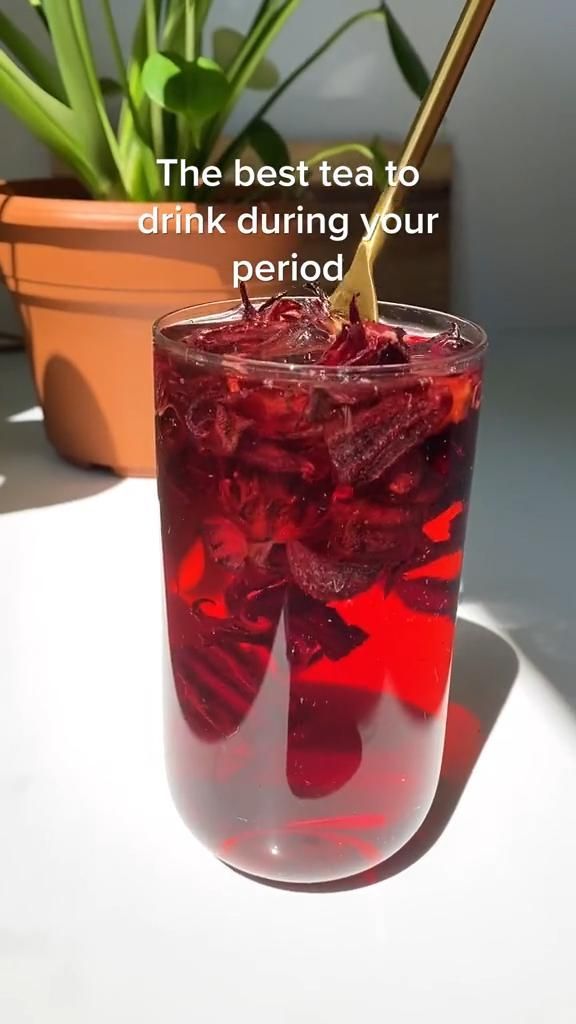 a glass filled with red liquid sitting on top of a table next to a potted plant