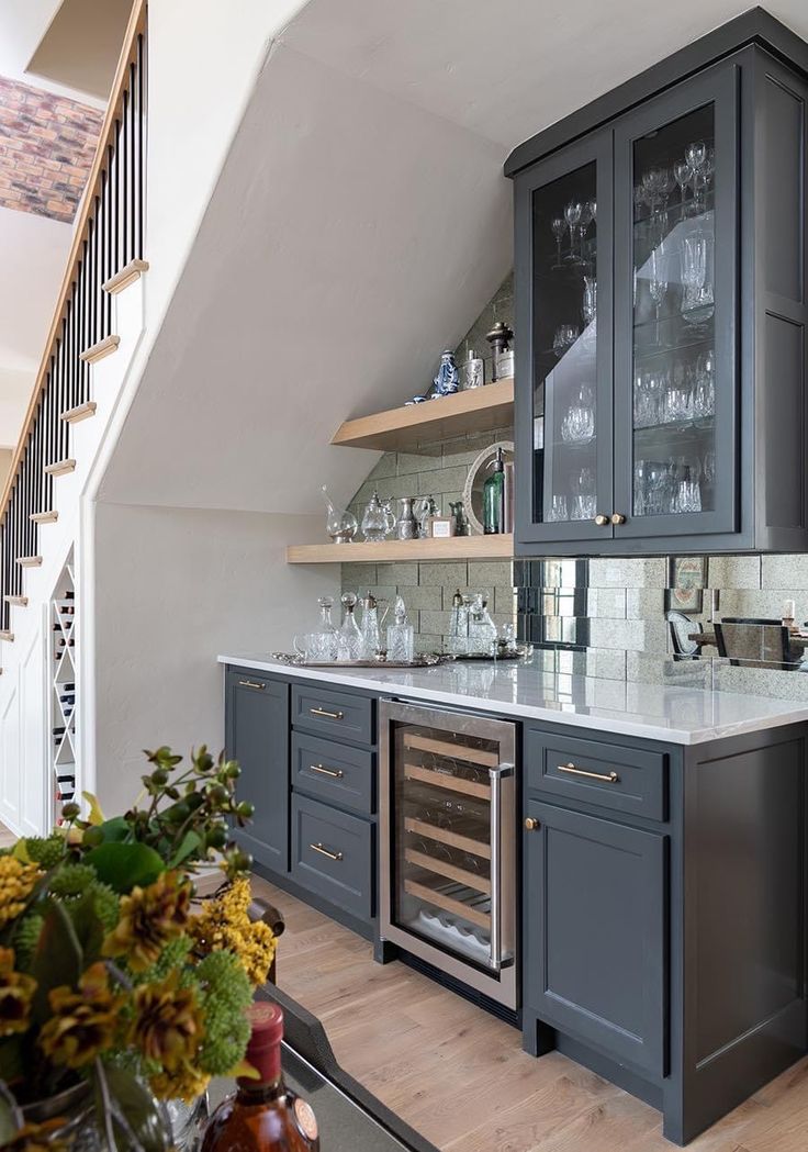 a kitchen with gray cabinets and marble counter tops, an oven in the center is surrounded by shelves that have wine glasses on them