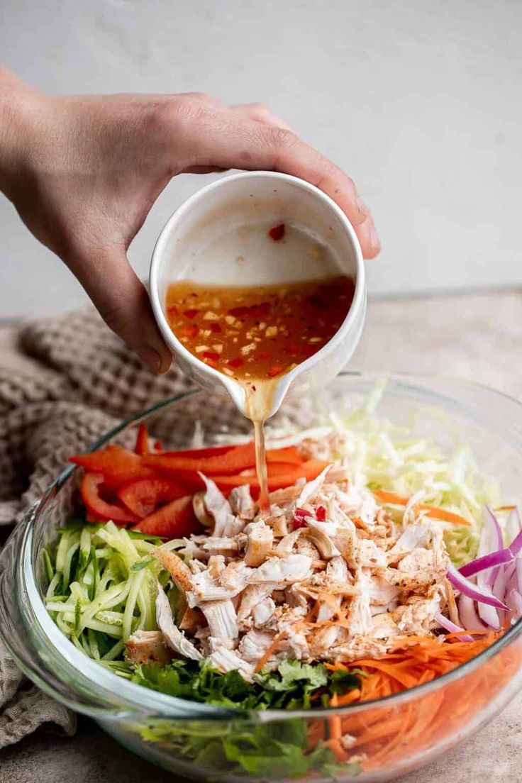 someone pouring dressing into a salad in a glass bowl with lettuce and carrots