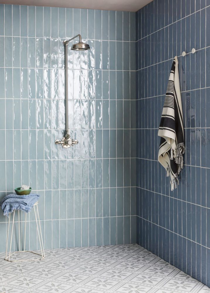 a blue tiled bathroom with a shower head and towel on the rack next to it