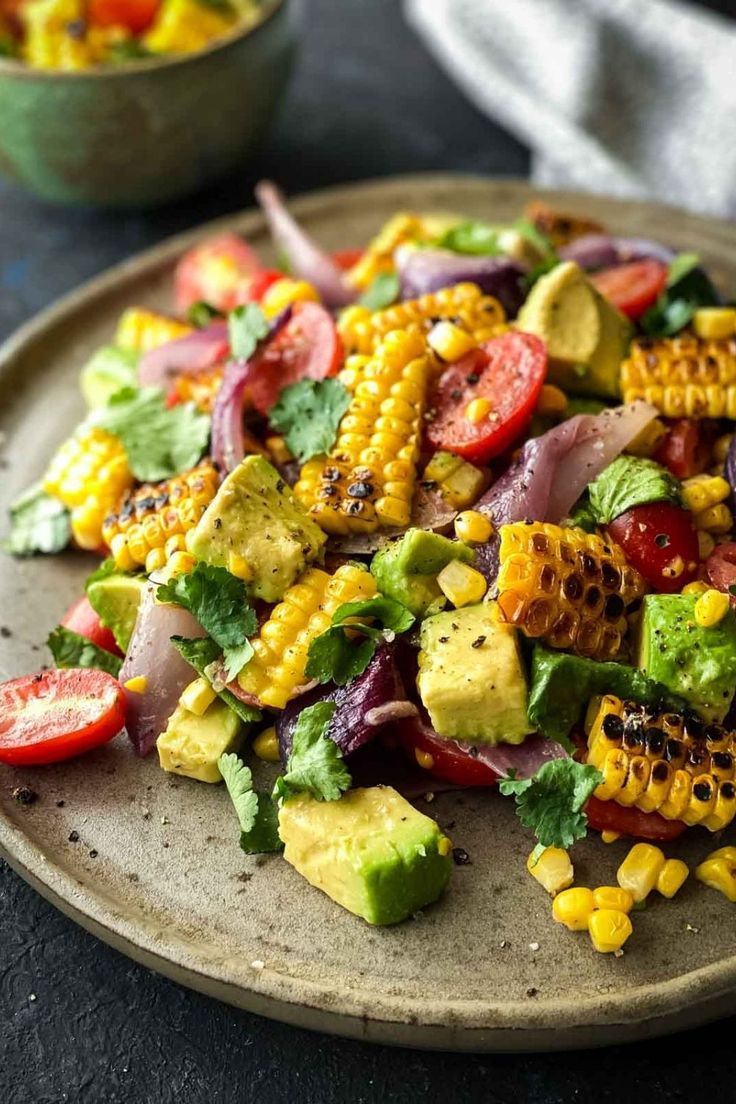 a plate filled with corn, tomatoes and avocado on top of a table