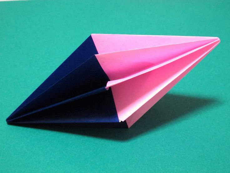 an origami paper airplane sitting on top of a green surface with pink and blue folds