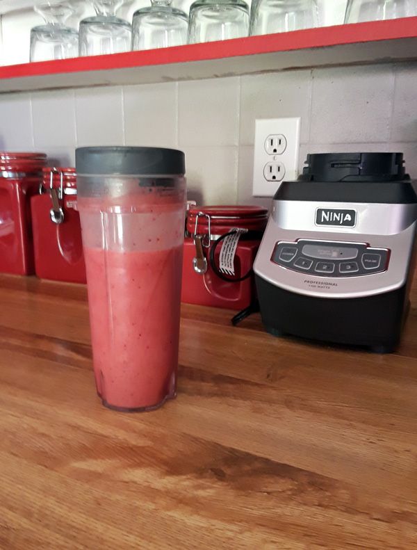 a blender sitting on top of a wooden counter next to a cup filled with liquid